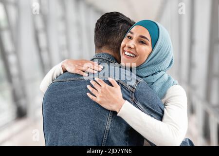 Bonne Réunion. Joyeuse femme musulmane dans hijab embrassant son mari à l'aéroport Banque D'Images