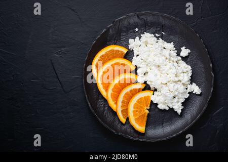 Fromage cottage à l'orange dans une assiette sur une table noire Banque D'Images