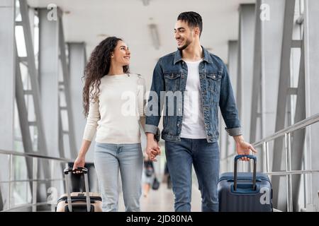 Portrait des conjoints romantiques du Moyen-Orient marchant avec des valises à l'Airport Hall Banque D'Images