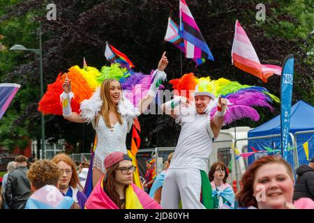 Homme et femme marchant sur pilotis avec boas en plumes arc-en-ciel et personne en costume argenté lors de l'événement Stoke gay Pride à Hanley Park le samedi 18th juin 2022 Banque D'Images