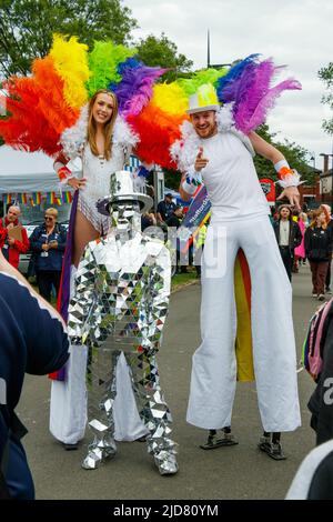 Homme et femme marchant sur pilotis avec boas en plumes arc-en-ciel et personne en costume argenté lors de l'événement Stoke gay Pride à Hanley Park le samedi 18th juin 2022 Banque D'Images