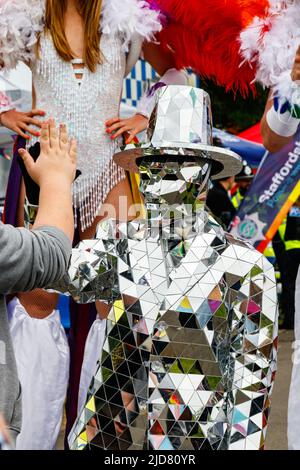 Homme et femme marchant sur pilotis avec boas en plumes arc-en-ciel et personne en costume argenté lors de l'événement Stoke gay Pride à Hanley Park le samedi 18th juin 2022 Banque D'Images