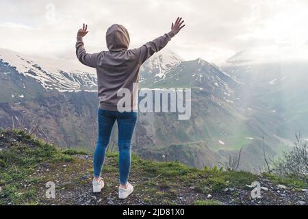Vue arrière d'une femme vêtue de vêtements décontractés levant les bras vers le haut en regardant un magnifique paysage de montagne le matin. Photo de haute qualité Banque D'Images