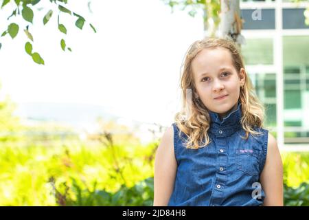 Belle adolescente souriante dans un chemisier bleu, contre un parc d'été vert. Banque D'Images