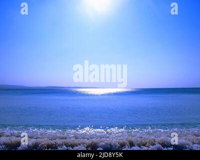 Vue sur l'océan dans un ciel bleu clair, rayons de soleil se reflétant sur l'eau, et une brise de vague qui vient. Banque D'Images