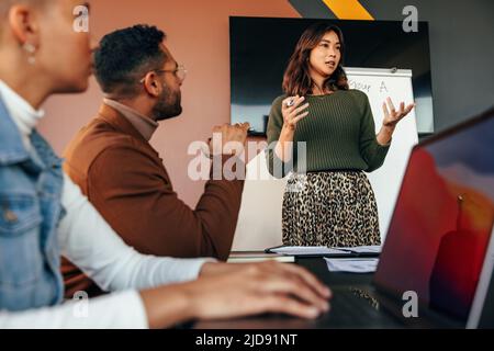 Une femme de direction donne une présentation dans une salle de réunion. Jeune femme d'affaires présentant sa stratégie d'affaires à ses collègues. Groupe d'entr. Multiracial Banque D'Images