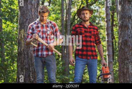 Deux bûcherons avec tronçonneuse et hache.Bûcheron mâle dans la forêt.Coupe-bois avec hache et bûcheron avec tronçonneuse. Banque D'Images