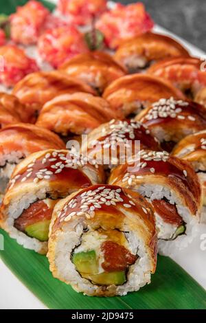 ensemble de différents petits pains à sushis maki colorés avec thon, saumon, crevettes, crabe et avocat et feuilles de bambou vertes dans une assiette en céramique blanche avec baguette, Banque D'Images