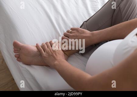 La femme enceinte s'assoit sur le lit, elle se moque de son pied gonflé Banque D'Images