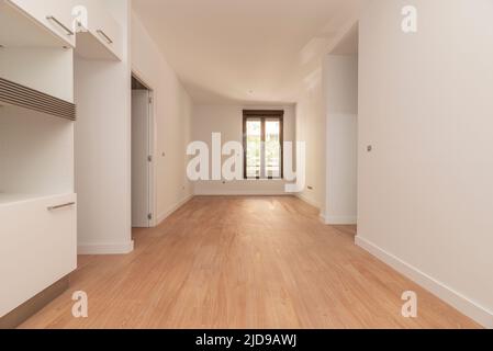 Appartement vide avec parquet clair, longue fenêtre en arrière-plan et murs peints en blanc Banque D'Images