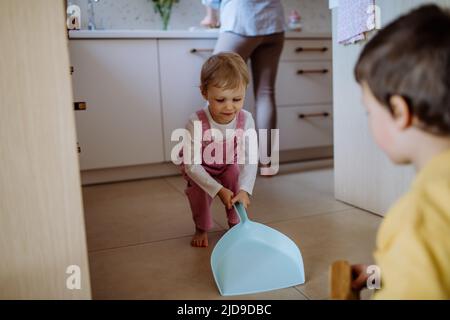 Un petit garçon et une petite fille qui aident à nettoyer la maison à l'aide d'une casserole et d'une brosse qui balaient la saleté du sol. Banque D'Images