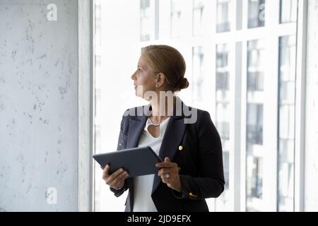 Une femme d'affaires d'âge moyen attirante qui se préoccupe de l'utilisation d'une tablette Banque D'Images