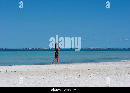 Une jeune femme marche le long de la mer en regardant son smartphone à la plage Isla Mujeres au Mexique Banque D'Images