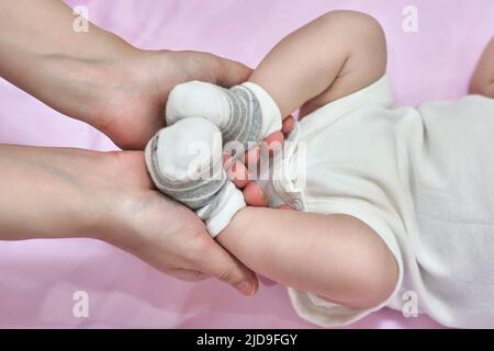 une femme met des chaussettes et une barboteuse pour bébé qui fait un massage des pieds à son petit enfant gros plan Banque D'Images