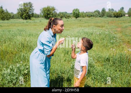 Les enfants d'âge préscolaire de maman et de fils passent du temps à l'extérieur en été et soufflent sur les pissenlits Banque D'Images