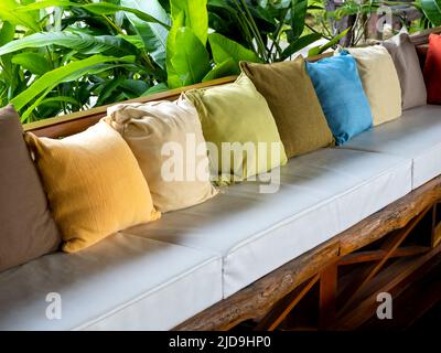 Rangée de nombreuses couleurs de décoration d'oreillers sur le siège en bois vintage avec des coussins blancs près du jardin vert. Banque D'Images