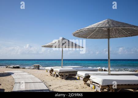 Chaises longues en bois avec parasols sur une plage tropicale. Banque D'Images