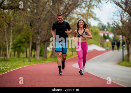 Jeune couple de sportifs en forme, garçon et fille courant tout en faisant de l'exercice sur les pistes rouges à l'extérieur Banque D'Images