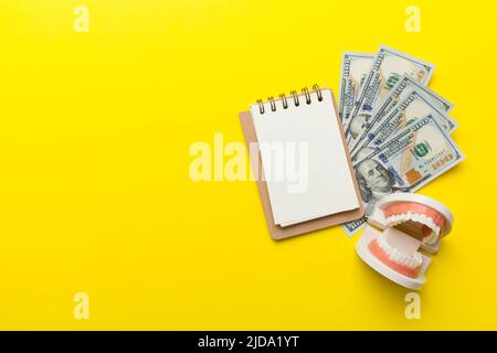 Composition de pose à plat avec modèle de typographie dentaire pédagogique et argent avec carnet sur table colorée, vue de dessus. Traitement coûteux. Banque D'Images