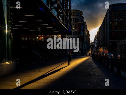 Une personne marche vers St Paul's à Londres dans un couloir lumineux tandis que le soleil se couche dans une rue vide le dimanche Banque D'Images