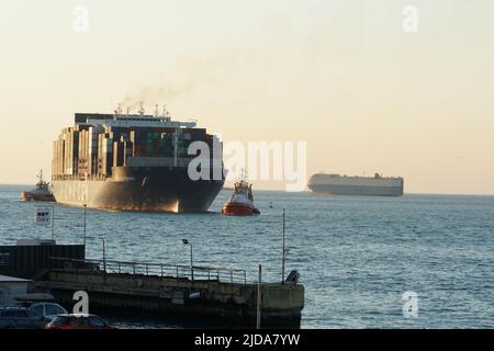 Koper, Slovénie - 04 16 2022: Énorme navire à conteneurs entièrement chargé de CMA CGM compagnie entrant dans le port de Koper pendant le coucher du soleil. Le navire est assisté par orange Banque D'Images