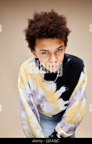 Portrait vertical d'un adolescent afro-américain portant une chemise à teinture par cravate et se penchant à l'appareil photo sur fond beige Banque D'Images