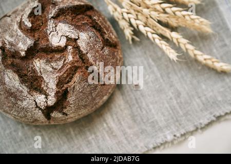 Vue de dessus de pain de seigle fraîchement cuit sur une entrée sans levure et sur un mélange de grain entier, de seigle et de farine de blé. Il se trouve sur une serviette, à côté d'une fleur séchée avec des grains. Mise au point sélective. Banque D'Images