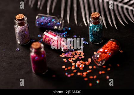 Bouteilles en verre avec confetti à paillettes sur fond noir avec décorations. Concept Noël et nouvel an. Mise au point sélective. Banque D'Images