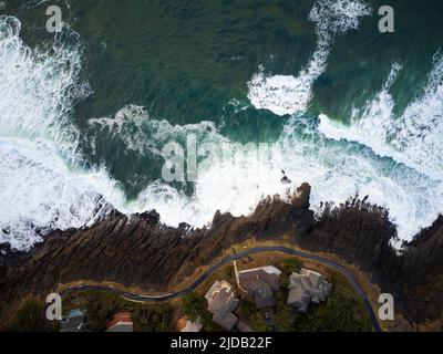 Vue de dessus. Petites maisons sur la côte verdoyante de l'océan. Des vagues de mousse blanche s'écrasont contre le rivage. Eau de mer turquoise. Solitude, romance Banque D'Images