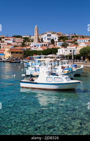 Gros plan de bateaux de pêche amarrés au bord de l'eau dans le port d'Emborio avec des bâtiments traditionnels et la tour de l'horloge dans le centre-ville sur Halki (CH.. Banque D'Images