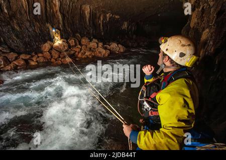 Les membres de l'équipe d'exploration grimpent contre la rivière qui se précipite dans la grotte de l'Ora alors qu'ils explorent les grottes sauvages et dangereuses du mont Nakanai... Banque D'Images