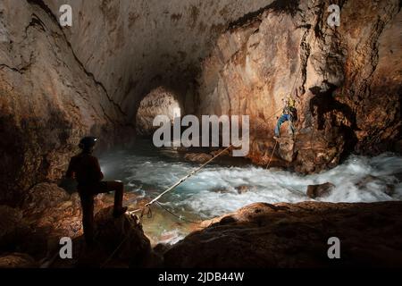 Les membres de l'équipe d'exploration grimpent contre la rivière qui se précipite dans la grotte de l'Ora alors qu'ils explorent les grottes sauvages et dangereuses du mont Nakanai... Banque D'Images