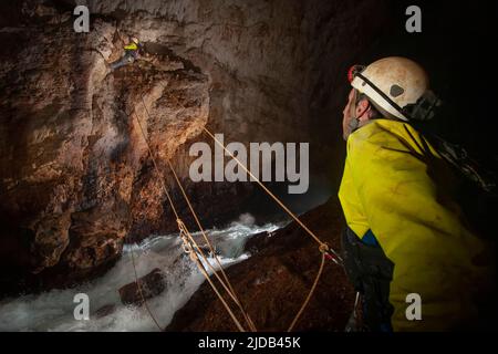 Les membres de l'équipe d'exploration grimpent contre la rivière qui se précipite dans la grotte de l'Ora alors qu'ils explorent les grottes sauvages et dangereuses du mont Nakanai... Banque D'Images