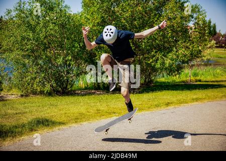 Jeune homme sur un sentier de parc avec un skateboard faisant un tour de bascule; Edmonton, Alberta, Canada Banque D'Images