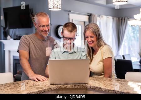 Jeune homme utilisant un ordinateur portable à la maison avec ses parents qui regardent; Edmonton, Alberta, Canada Banque D'Images