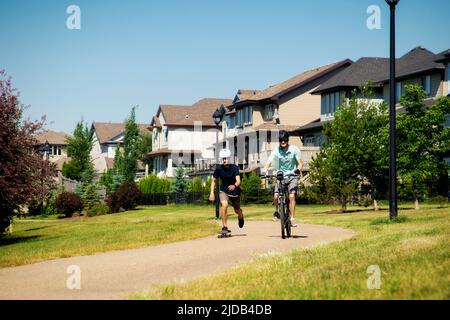 Frères qui passent du temps ensemble dans le quartier, un sur un vélo et un sur un skateboard; Edmonton, Alberta, Canada Banque D'Images