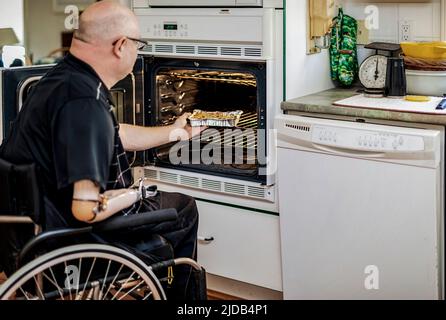Homme avec des amputations de deux membres utilisant le four dans la cuisine à la maison; St. Albert, Alberta, Canada Banque D'Images