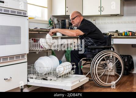 Homme avec des amputations de deux membres chargeant le lave-vaisselle dans la cuisine à la maison; St. Albert, Alberta, Canada Banque D'Images