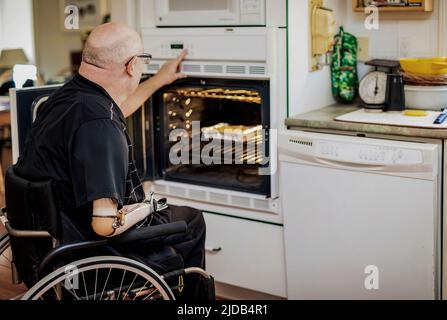 Homme avec des amputations de deux membres utilisant le four dans la cuisine à la maison; St. Albert, Alberta, Canada Banque D'Images