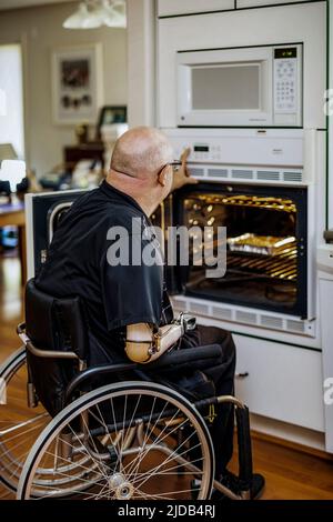 Homme avec des amputations de deux membres utilisant le four dans la cuisine à la maison; St. Albert, Alberta, Canada Banque D'Images