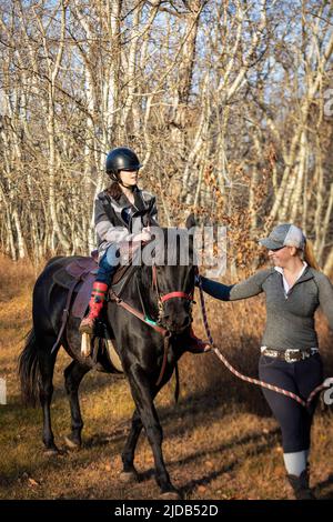 Une jeune fille atteinte de paralysie cérébrale et son entraîneur travaillant avec un cheval sur un sentier lors d'une séance d'hippothérapie ; Westlock, Alberta, Canada Banque D'Images