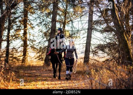Une jeune fille atteinte de paralysie cérébrale et son entraîneur travaillant avec un cheval sur un sentier lors d'une séance d'hippothérapie ; Westlock, Alberta, Canada Banque D'Images