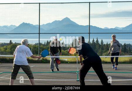 Les seniors, hommes et femmes, jouent au Pickleball en plein air à l'école secondaire Homer avec les montagnes Kenai et la baie de Kachemak en toile de fond Banque D'Images