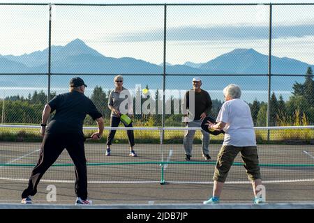 Les seniors, hommes et femmes, jouent au Pickleball en plein air à l'école secondaire Homer avec les montagnes Kenai et la baie de Kachemak en toile de fond Banque D'Images