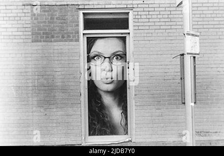 Le visage de la femme qui se trouve dans une petite fenêtre d'un édifice en briques; Winnipeg, Manitoba, Canada Banque D'Images