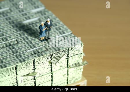 Miniature jouets personnes photographie conceptuelle. Couple âgé se tenant au-dessus de pile d'argent liquide. Concept de finance et d'épargne. Photo d'image Banque D'Images