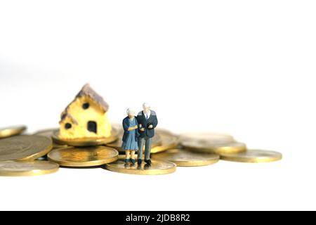 Miniature jouets personnes photographie conceptuelle. Couple âgé se tenant au-dessus de la pile de pièces d'argent pour le logement. Isolé sur fond blanc. Photo d'image Banque D'Images