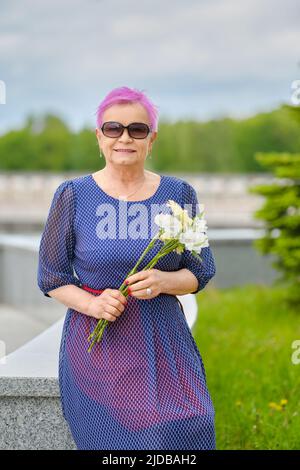 Portrait d'une femme mûre souriante aux cheveux roses courts debout près du sapin dans la rue Banque D'Images