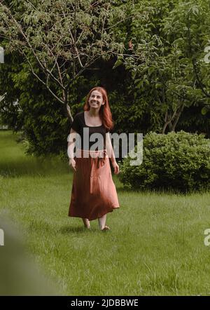 Joyeux cheveux de gingembre femme marchant pieds nus dans le parc ou le jardin. Liberté et mode de vie sain. Femme dans son 40s ayant le repos à l'extérieur. Personnes dans Banque D'Images