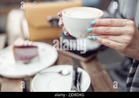 Gros plan d'une tasse de cappuccino dans les mains des femmes avec une manucure bleue. Café-restaurant extérieur. Banque D'Images